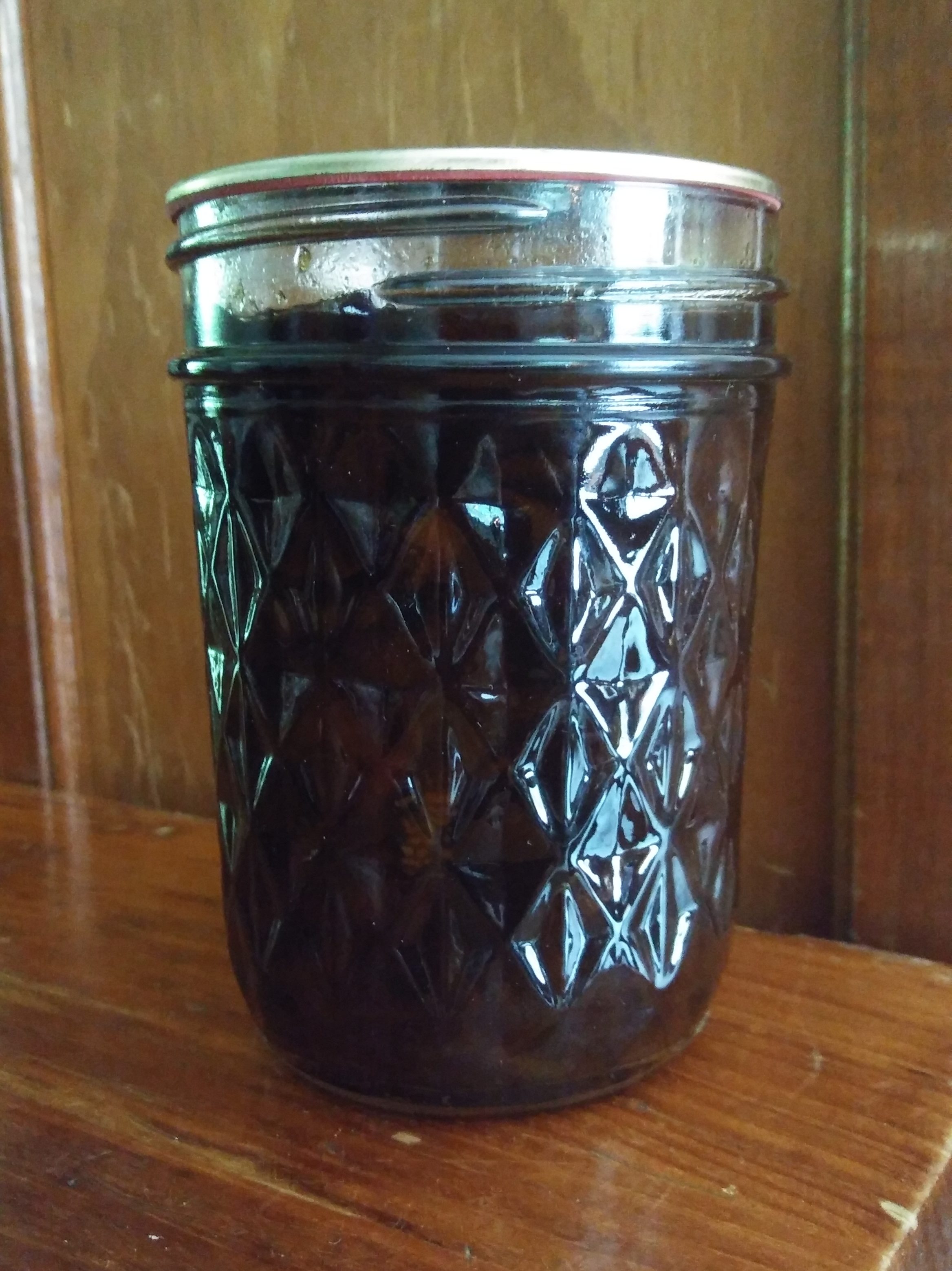 Jar of jelly sitting on an old, wooden table in a kitchen.